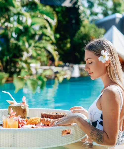 Female tourist in luxurious hotel enjoys swimming pool and tropical food