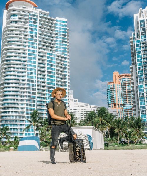 Hipster man with luggage bag on wheels standing on the south beach in miami.