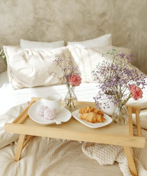 View of a wooden tray with breakfast in bed in a hotel room.